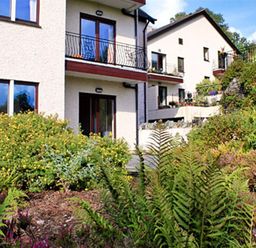 The exterior of a two story house with balconies and a garden with various plants and bushes at Romney 12 in Waterhead near Ambleside