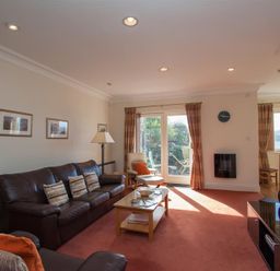 A living room with leather sofas coffee table TV and glass doors leading to a garden at Romney 12 Waterhead near Ambleside