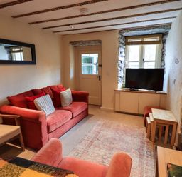 A living room with two red sofas a wooden chair a television on a cabinet a wooden door and a window with stone framing at Penny Red Cottage in Ambleside