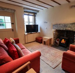 A living room with a red sofa red armchair a TV on a cabinet a stone fireplace with a wood burning stove and nested tables at Penny Red Cottage in Ambleside