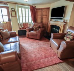 A living room with leather sofas a red rug a window seat and a wall mounted television at Heron Cottage in Ambleside