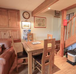 A dining area with a wooden table and four chairs next to a leather sofa and wooden staircase at Heron Cottage in Ambleside