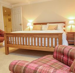 A bedroom with a wooden bed with striped pillows two lamps on wooden nightstands and plaid chairs at The Miller in Ambleside