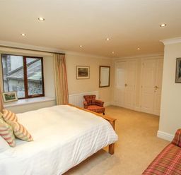 A bedroom with a bed white bedding and striped pillows a window with curtains two armchairs and framed pictures on walls at The Miller in Ambleside