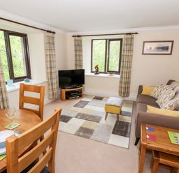 A living room with a sofa a small dining table with chairs a television on a stand and windows with curtains at Waterfalls in Ambleside