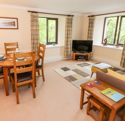 A living room with a wooden dining table and chairs a sofa a TV on a stand and two windows with curtains at Waterfalls Ambleside