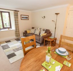 A living room with a sofa pillows a floor lamp wooden dining table set with dishes and wine bottle at Waterfalls in Ambleside