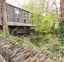 A stone house with a wooden balcony surrounded by trees and a stone wall with ivy at Waterfalls in Ambleside