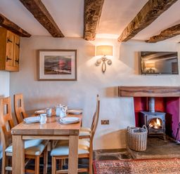 A dining area with wooden table and chairs set with dishes next to a fireplace with a wood-burning stove and wall-mounted TV at Knotts Cottage in Troutbeck