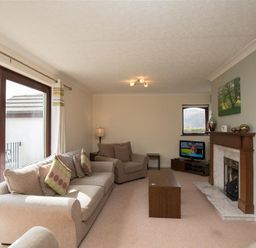 A living room with beige sofas, wooden coffee table, fireplace, television, and large window with curtains at Todd Crag in Ambleside