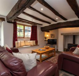 A living room with exposed wooden beams a wood burner two leather sofas a wooden coffee table and a window seat at Lowfold Cottage in Ambleside