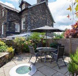 An outdoor patio area with a round table and chairs under a large umbrella next to a stone house at Lowfold Cottage in Ambleside