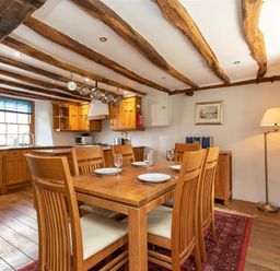 A dining area with wooden table and chairs set with plates and glasses adjacent to a kitchen with wooden cabinets and hanging pots at Lowfold Cottage in Ambleside