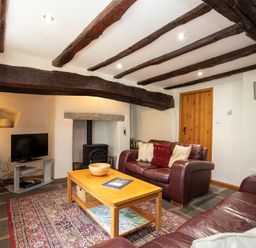 A living room with wooden beams on the ceiling leather sofas a wooden coffee table a television and a stove at Lowfold Cottage in Ambleside