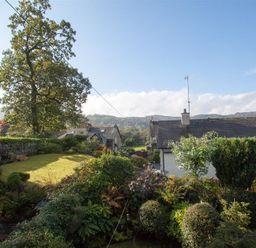 A garden with various bushes and trees near houses under a clear sky at Sunset Cottage in Ambleside