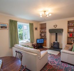 A living room with two sofas a small TV a wood stove and bookshelves at Sunset Cottage in Ambleside
