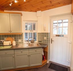 A kitchen with green cabinets a stainless steel sink a kettle toaster and a white door with window panels at Sunset Cottage in Ambleside
