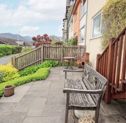 A garden patio with a wooden bench table and chairs beside a wooden fence at Fellcroft in Troutbeck