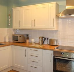 A kitchen with white cabinets stainless steel appliances and wooden countertops at Four Seasons Cottage in Ambleside