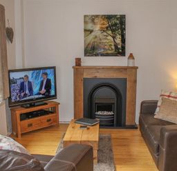 A living room with a television on a wooden stand a fireplace with a wooden mantel brown leather sofas and a wooden coffee table at Four Seasons Cottage in Ambleside