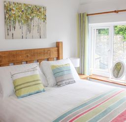 A bedroom with a wooden bed frame striped pillows and blanket a window with curtains and a mirror on the sill at Four Seasons Cottage in Ambleside