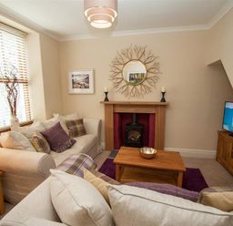 A living room with cream sofas a wooden coffee table and a fireplace at Acorn Cottage in Ambleside