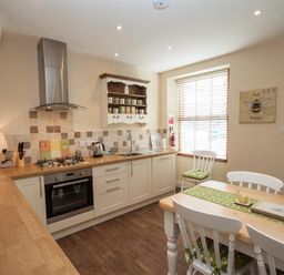 A kitchen with wooden countertops white cabinets a dining table with chairs and a window with blinds at Acorn Cottage in Ambleside