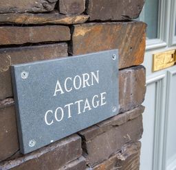 A stone wall with a plaque reading Acorn Cottage next to a door with a mail slot at Acorn Cottage in Ambleside