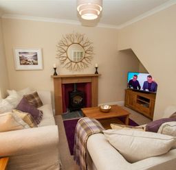 A living room with two beige sofas a wooden coffee table a fireplace and a television at Acorn Cottage in Ambleside
