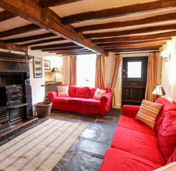 A living room with red sofas wooden ceiling beams a fireplace and a striped rug at Rock Cottage in Ambleside