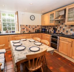 A kitchen with wooden cabinets a dining table set with plates and glasses and a window with wooden shutters at Rock Cottage in Ambleside