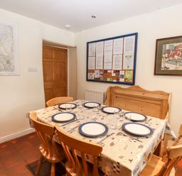 A dining table set with plates glasses and cutlery surrounded by wooden chairs and a bench in a room with a map and framed pictures on the walls at Rock Cottage Ambleside
