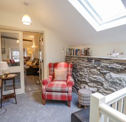 A seating area with a red armchair and plaid footstool next to a stone wall with books and ceramic ducks at Highfold in Ambleside