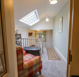 A hallway with a plaid armchair a wooden chest a skylight window and framed pictures on the wall at Highfold Ambleside