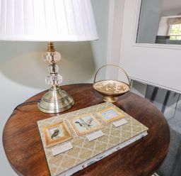 A wooden table with a lamp a decorative book and a small bowl in a room with a window at Highfold in Ambleside