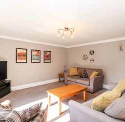 A living room with sofas cushions a wooden coffee table TV and framed pictures on the wall at Ghyll View in Ambleside