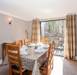 A dining room with a table set for six near a balcony with outdoor furniture at Ghyll View in Ambleside