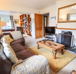 A living room with a brown leather sofa a wooden coffee table a fireplace a TV and a bookshelf at Rawfell in Great Langdale