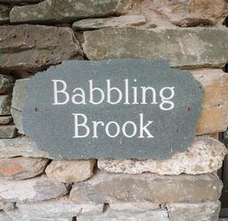 A stone plaque with the words Babbling Brook mounted on a stone wall at Babbling Brook in Ambleside