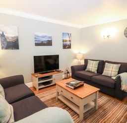 A living room with two sofas a coffee table a television and landscape pictures on the wall at Babbling Brook Ambleside