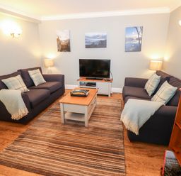 A living room with two sofas a wooden coffee table a television and a bookcase at Babbling Brook in Ambleside