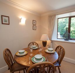 A dining area with a round wooden table set for four next to a window with a vase on the sill at Over Ghyll in Ambleside