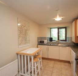 A kitchen with a small table and two stools a microwave on the counter a window above sink and tiled floor at Over Ghyll Ambleside