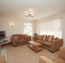 A living room with brown sofas a wooden coffee table a television and vertical blinds on windows at Bield How in Ambleside