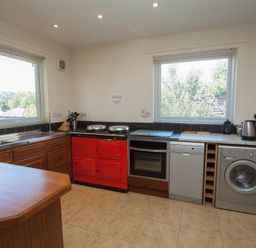 A kitchen with a wooden countertop a red stove oven dishwasher washing machine and two windows at Bield How in Ambleside