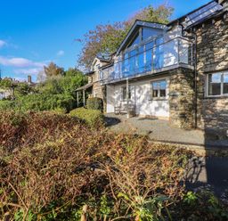 A stone house with a balcony and bushes in front at Garden House Ambleside