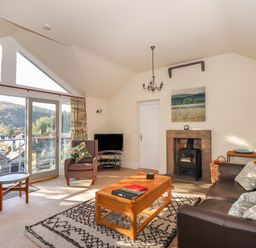 A living room with a sofa an armchair coffee table fireplace and windows showing a hillside view at Garden House in Ambleside