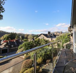A balcony with metal chairs overlooking a residential area with stone houses and hills at Garden House in Ambleside