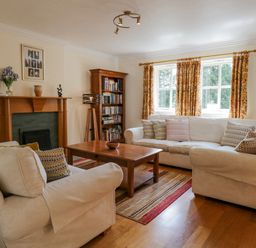 A living room with two beige sofas a wooden coffee table a fireplace and a bookshelf at Orchard House in Ambleside