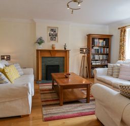 A living room with two white sofas a wooden coffee table a rug a wooden bookshelf and a fireplace at Orchard House Ambleside